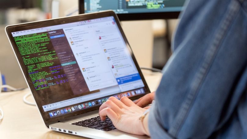 Photo of the laptop screen of a Capital One team member, showing a window with code and a Slack messaging window.